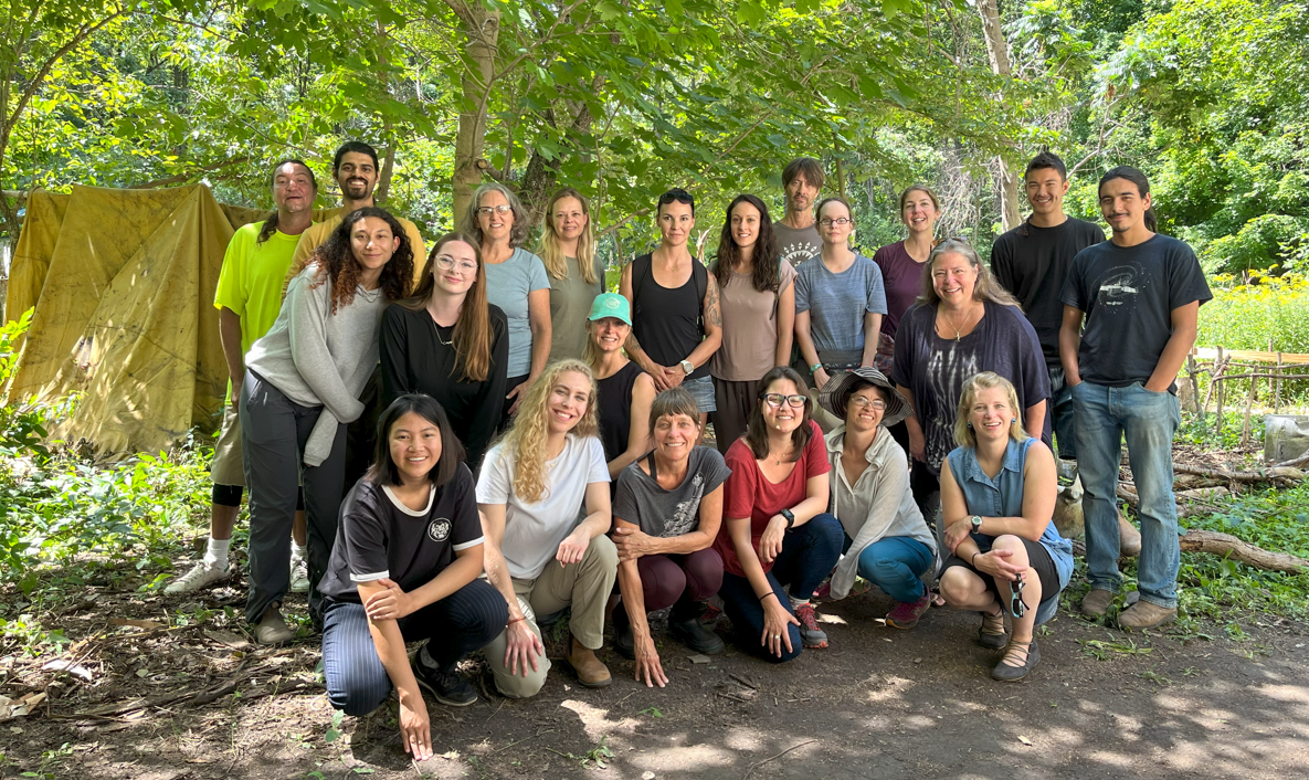 People gathered in a group in a forest to smile for the picture. Tent in the background. 