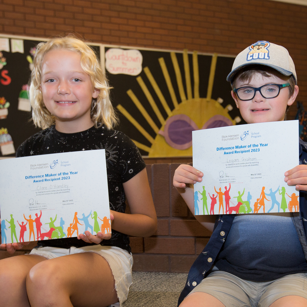 Deux enfants sont assis et tiennent des certificats « Personne qui fait une différence de l’année  ».