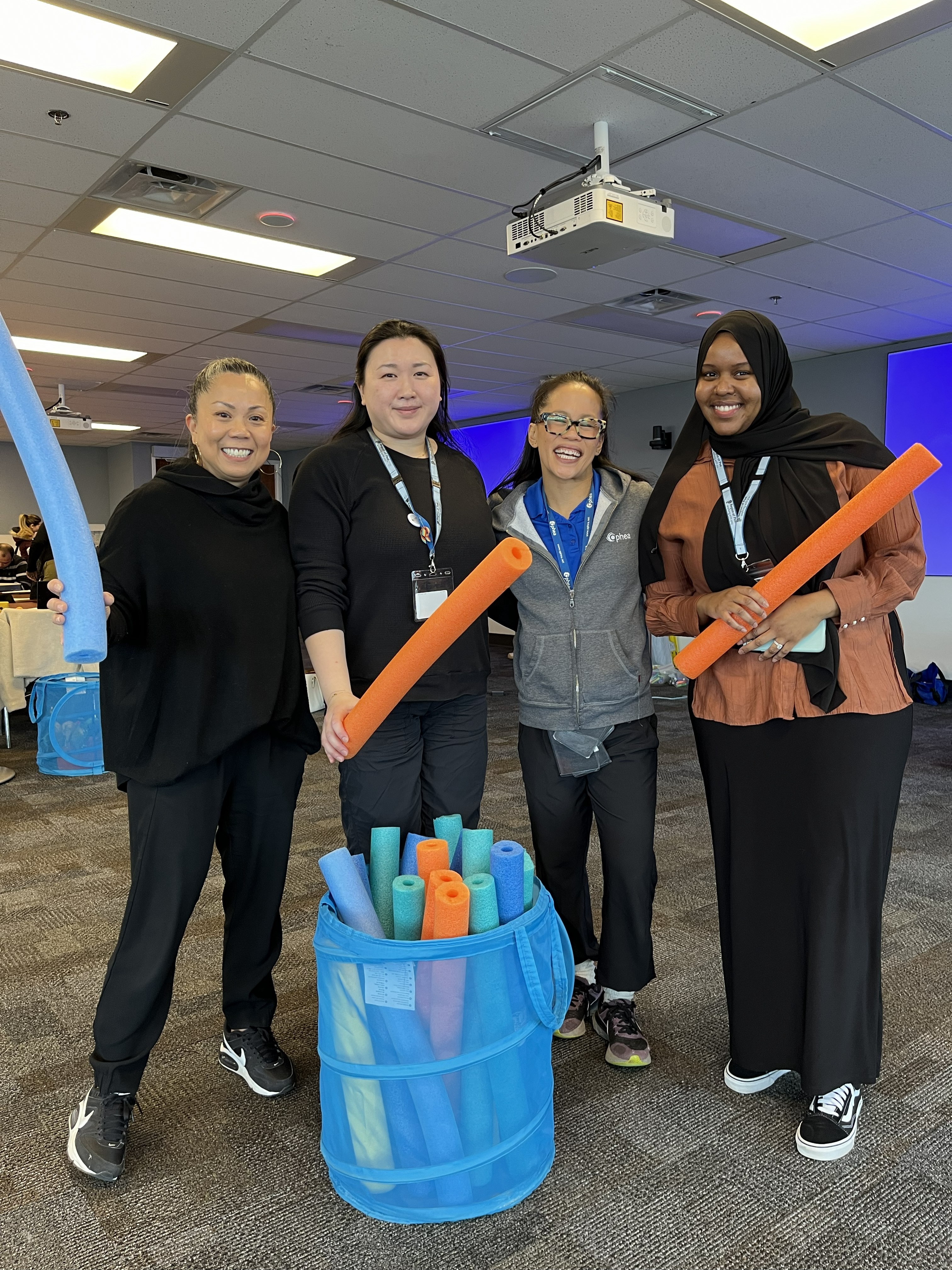 Three members of the Peel Public Health team, with an Ophea workshop leader. They are smiling at the camera and holding pool noodles.