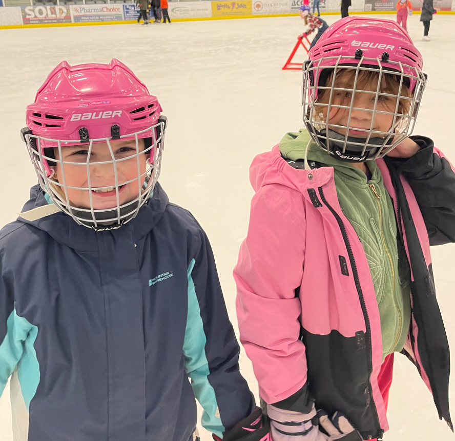 Two students from Nouvel Horizon elementary school on an ice rink. They are wearing helmets and winter jackets.