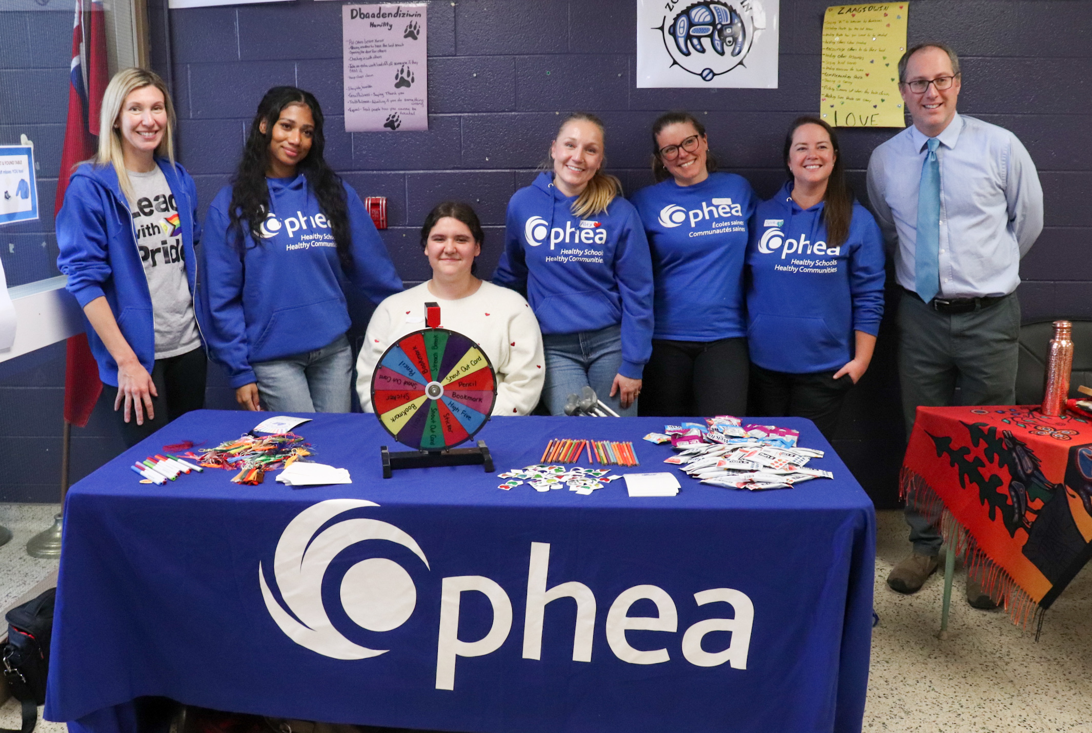 Un groupe de personnes souriantes se tenant derrière le stand d'Ophea à l'école secondaire de Parry Sound.