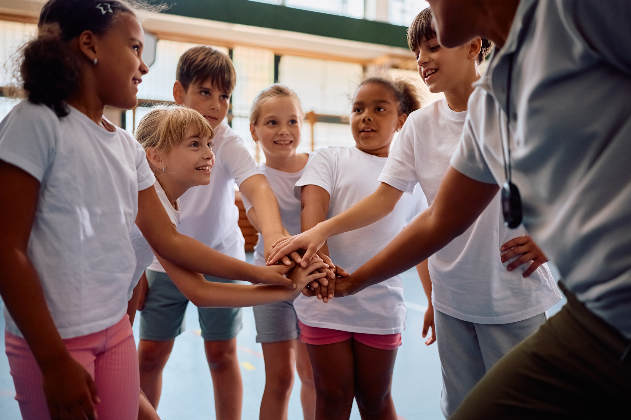 Happy kids and their coach joining hands in unity during Physical Education class