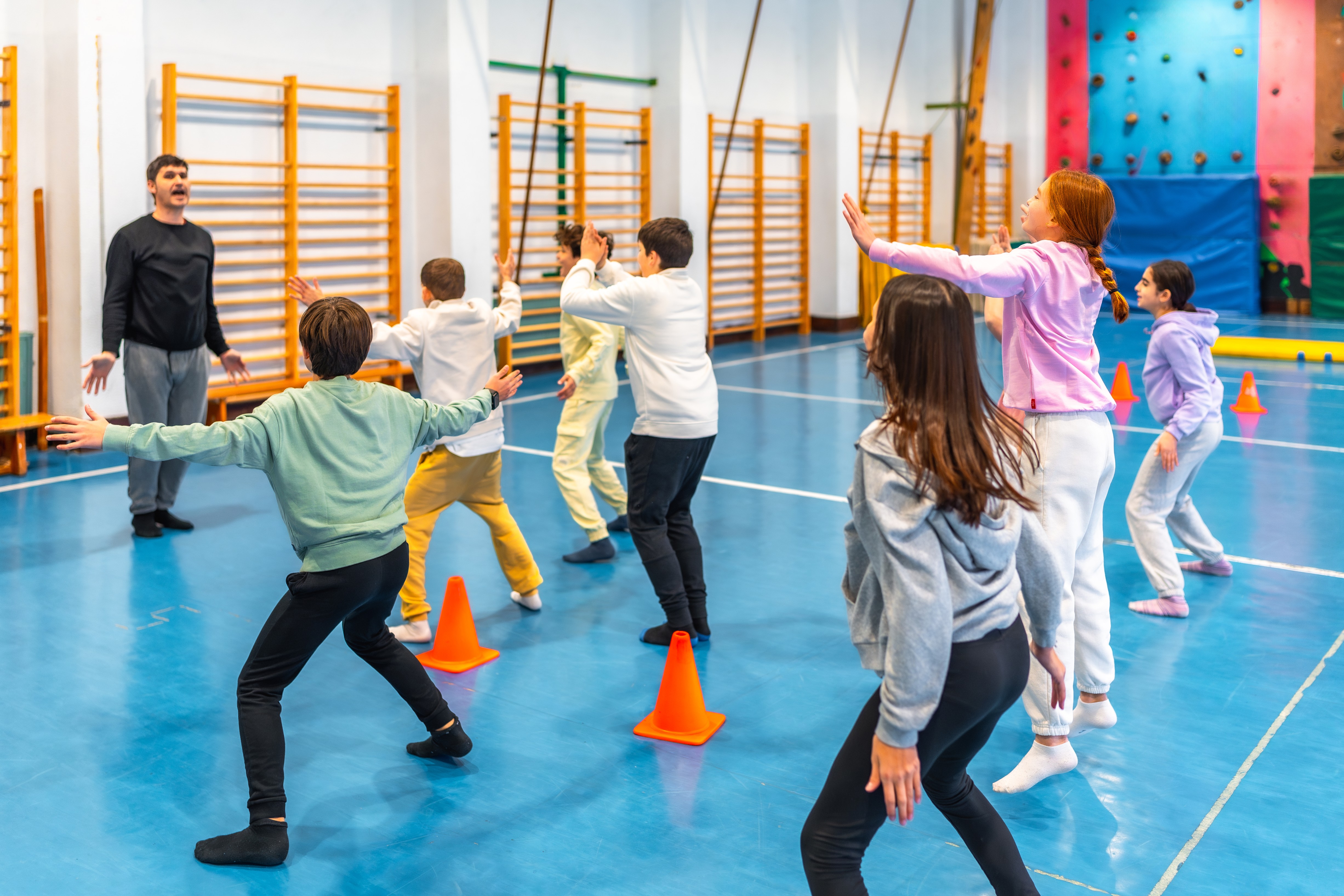 Un groupe d'élèves du primaire faisant des exercices de gymnastique dans le gymnase de leur école, sous la direction d'un enseignant.
