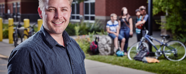 Dr. Scott Leatherdale, COMPASS Principal Investigator, a white male standing outdoors in front of a school and a group of four students, two who have bikes who are talking.