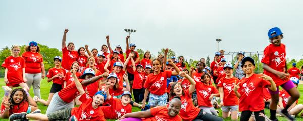 A large, diverse group of student athletes wearing red Toronto Blue Jays jerseys gather on a field for a team photo.