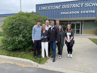 Lara Paterson, a white woman with blond hair and Ophea's 2023-2024 Award of Distinction recipient stands with a group of people including Chris Markham, Ophea Executive Director & CEO, outside the Limestone District School Board Education Centre.